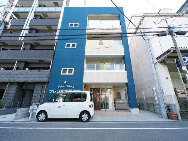 青い建物の外観 ルーフバルコニ 新しい外観の建物前に白い車が停まっており、清潔感のあふれるエントランスがお出迎えします。通りに面しており、アクセスも良好です。