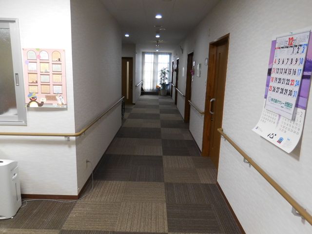 清潔感のある施設の廊下 廊下1 壁にはカレンダーが掲示され、日々の予定管理が行き届いています。手すり付きの廊下が、安心して歩行できる環境を提供しています。