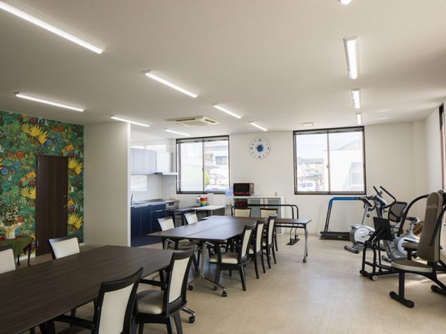 機能訓練室と食卓のある部屋 機能訓練室   明るい窓辺にテーブルと椅子が並び、運動機器も置かれています。食事や体を動かす時間を過ごしやすい空間です。