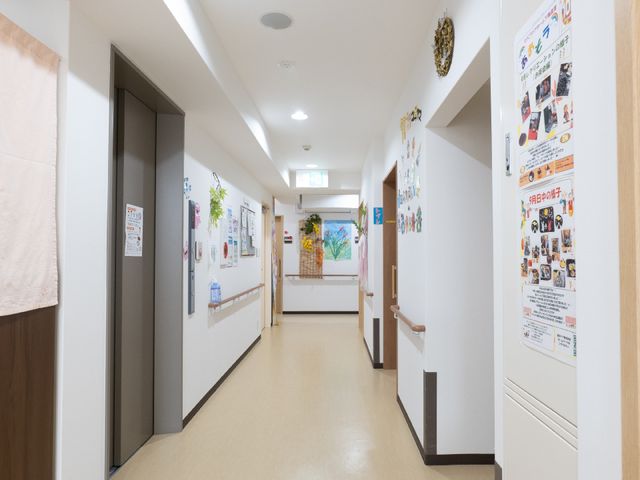 広々とした明るい廊下 廊下 広く明るい通路は清潔感があり、壁には様々な掲示物が見られます。利用者の皆様の日々の活動や思い出が壁一面に飾られており、温かな雰囲気が感じられます。