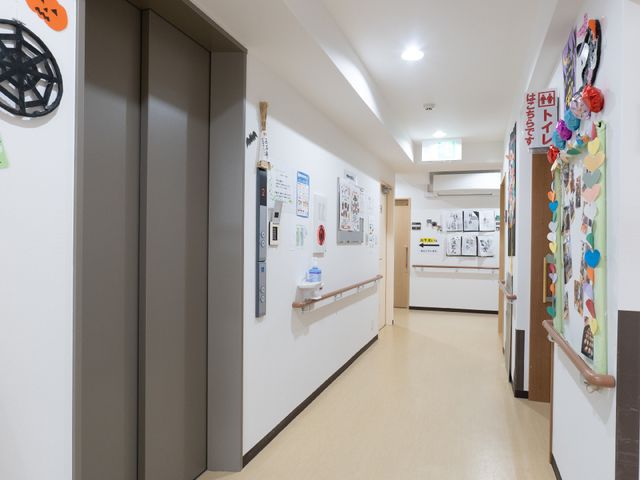 廊下の明るく清潔な様子 エレベーター 手すりが設置された広々とした廊下。壁に飾られた掲示物が、明るい雰囲気を演出しています。