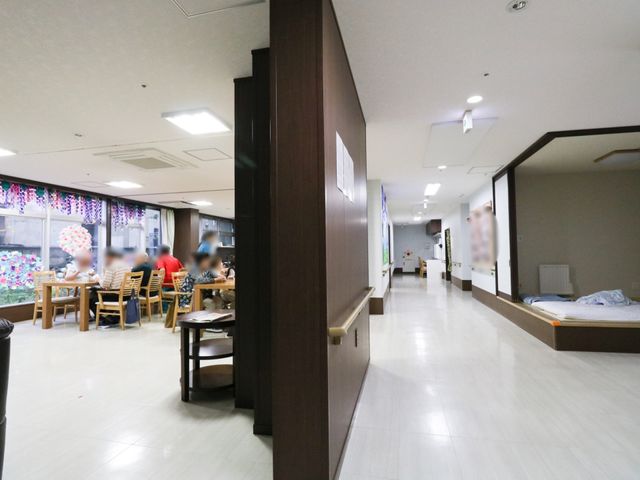 廊下と食堂の様子 共有スペース ゆったりとした空間で食事を楽しむ人々が映っており、家庭的な雰囲気が漂っています。廊下は明るく清潔感があり、快適に過ごせる設計になっています。