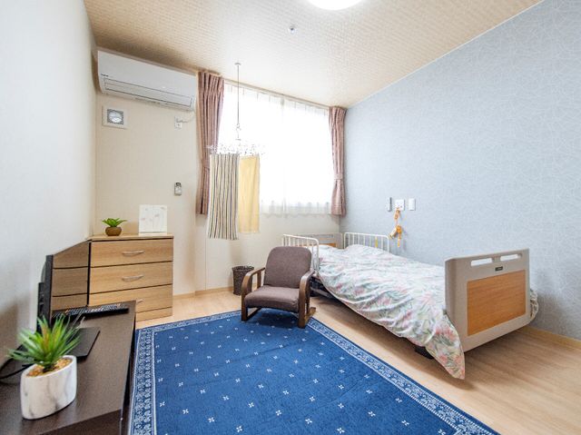 居心地の良い個室風景 地域交流 ゆったりとした個室で、落ち着いた色合いのカーテンが窓辺の光を柔らかくしています。必要な家具が整い、プライベートな時間を大切にできる空間です。