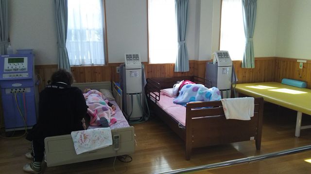 居室の日常風景 居室 ゆったりとした居室で、看護師が一対一でケアを行っています。窓辺の明るさが心地よい空間を演出しています。