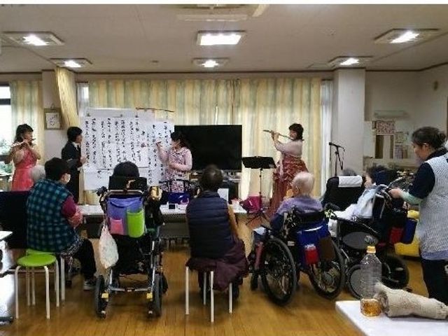 多目的室での活動風景 サポート 椅子に座る方々が集い、楽器の演奏や歌に合わせて活動をしている和やかな空間です。日々の生活に潤いと楽しさを提供する場所となっています。