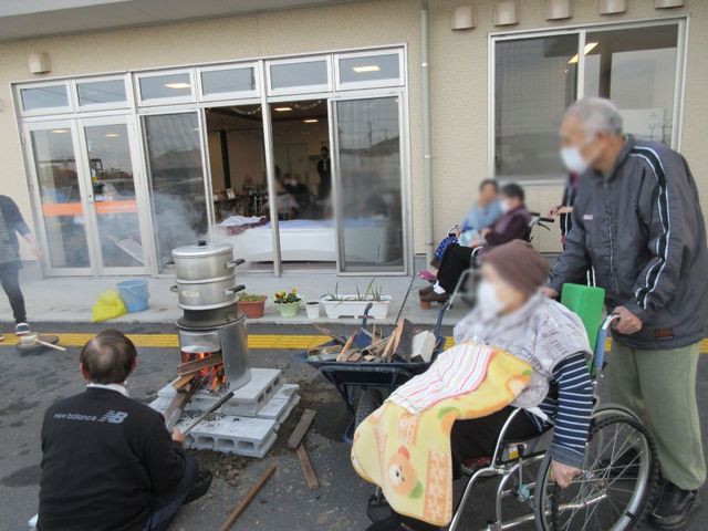 屋外での催し 外観 温かな雰囲気の中、車椅子の方も楽しめる屋外イベントが開催されています。薪を使った調理中です。
