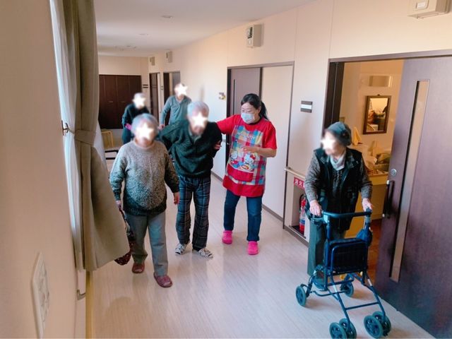 スタッフと利用者の様子 廊下 明るい廊下でスタッフと利用者が一緒に歩いています。丁寧なサポートが感じられます。