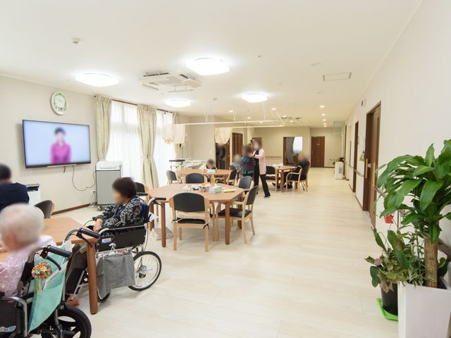 共有スペースの明るい居室 共有スペース ゆったりとしたラウンジで、居住者が椅子に座ってテレビを楽しんでいます。穏やかな雰囲気があり、共に時間を過ごせる場所です。