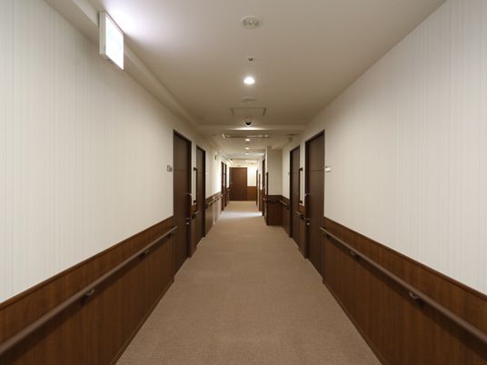 廊下の壁には、横長の手すりが設置されており、居室と居室の間の壁にも、I字の手すりが付いている。ドアの横には、ネームプレートがある。