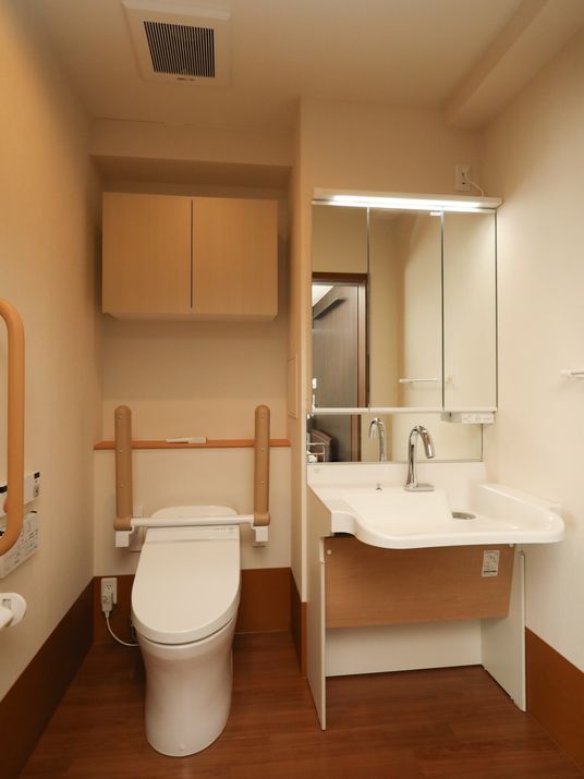 トイレの横にある洗面台の下は、物がなく広いスペースがある。便座の上には、木目のドアの付いた収納棚が設置されている。