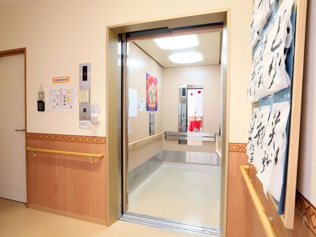 エレベーター付近の通路 エレベーター 明るく清潔感のある廊下はゆったりとした作りで、壁には書道の作品が飾られています。動線を大切にした設計で、利用者の快適な移動が考慮されています。