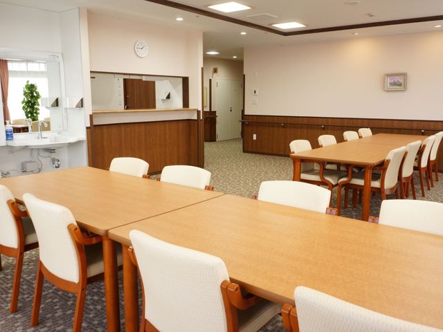 温かみのある共有スペース 食堂 ゆったりと配置されたテーブルと椅子が特徴のダイニングエリアです。職員対応可能なフロントも設置され、コミュニケーションが図れる設計になっています。