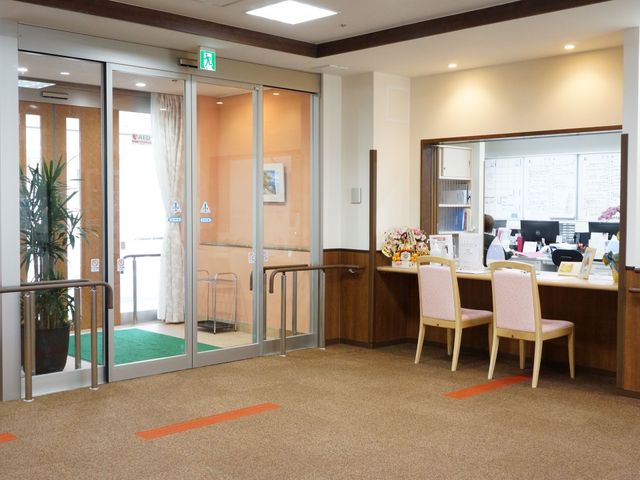 エントランスと受付の風景 玄関 木目調の温かみのあるフロントでは、笑顔でスタッフが迎えてくれます。ご来訪者はゆとりのある空間で対応を待つことができます。