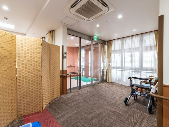 明るい廊下の一角 玄関ホール ゆったりとした空間の廊下には、歩行をサポートする手すりが完備されており、日差しの差し込む窓辺で明るく快適な通路を実現しています。