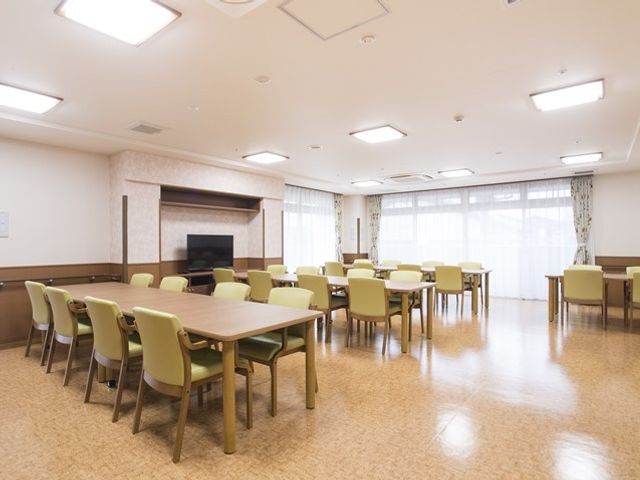 広々とした明るい食堂 食堂兼機能訓練室 広々とした食堂では、テーブルと椅子が整然と配置され、共に食事の時間を楽しむことができます。窓からは自然光が入り、居心地の良い雰囲気を醸し出しています。