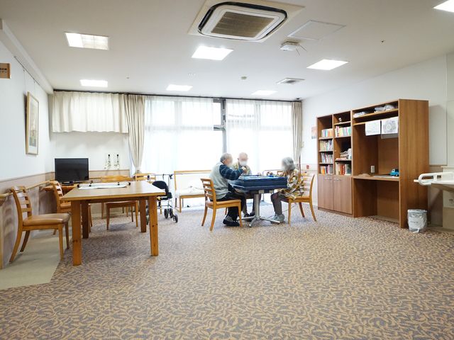 共有スペースの様子 共有スペース 木製のテーブルを囲んで、ゲームを楽しむ方々がおられます。書籍やテレビも備えた、くつろぎのスペースが広がっています。