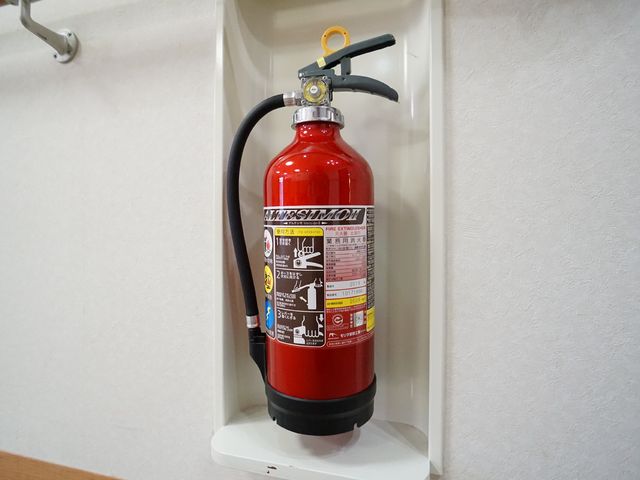 壁掛け消火器 消火器 きちんとメンテナンスされた消火器が壁に取り付けられています。就業先として、安全面への配慮が行き届いている様子が伺えます。