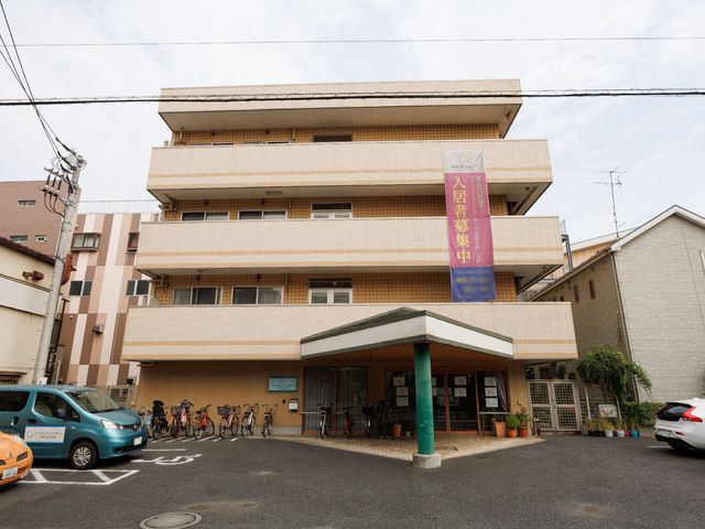 多階層の建物の外観 外観 ゆとりあるエントランスを備えた、落ち着いた色合いの建物です。ここでは日々の業務を通じて多くの人々のサポートが行われています。