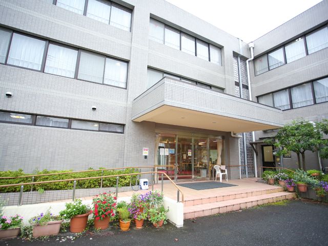 快適なエントランス外観 外観 ガラス張りで解放的な雰囲気のエントランスです。花々に囲まれ、訪れる方々を明るく迎えます。