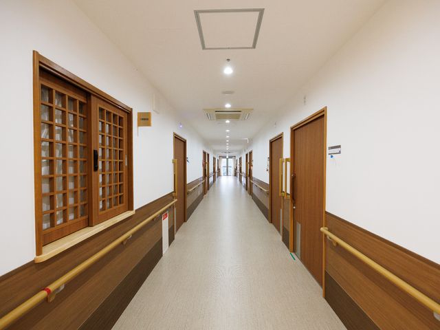 清潔な施設の廊下 廊下 手すりが設置された明るい通路です。木目調の装飾が温かみのある空間を演出しており、静かな環境が保たれています。