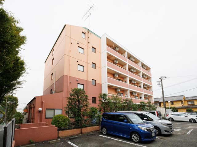 ピンク色の建物外観 外観 ゆったりとした駐車スペースが確保された落ち着いた色合いの建物です。周辺環境に溶け込むデザインが特徴です。