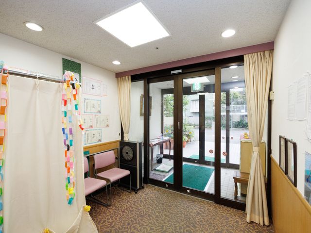 中庭へ続く出入口 玄関 中庭へと続く開放的な出入口は明るく、居心地の良い空間を提供しています。清潔感溢れる待合スペースは、訪れる方々に安らぎを与えます。