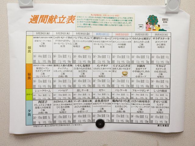 掲示された週間食事表 献立表 充実したメニューを提供する食事の週間スケジュールが掲示されています。栄養バランスを考慮した多彩な料理で、日々の暮らしが豊かになります。