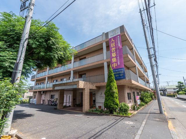 明るい日差しの多層建築 外観 落ち着いた色合いの建物が、周囲の緑と調和しています。施設の周囲は整備されており、開放感があります。