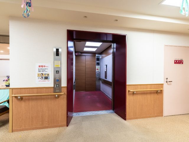 赤い扉のエレベーター前 エレベーター 手すり付きでバリアフリーに配慮された明るいエレベーターホールです。スタッフも利用しやすい設計になっており、業務の効率化に貢献します。