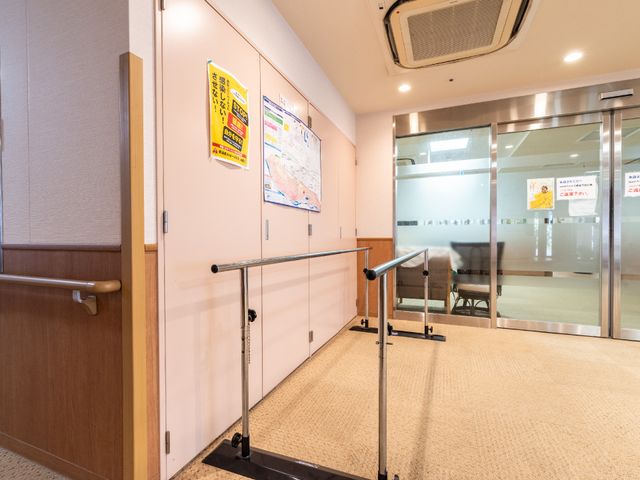 廊下と掲示物を備えた空間 玄関 掲示物が並ぶ、手すり付きの安全に配慮した廊下です。清潔でゆとりあるこの通路は、日々の快適な移動に貢献します。