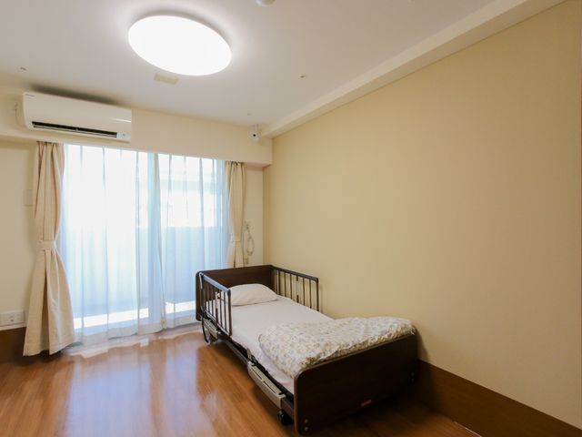 清潔な居室の一角 居室 温かみのある木目調の床と、落ち着いた色合いのカーテンが特徴的な居室です。個人のプライバシーも配慮された、快適な空間となっています。