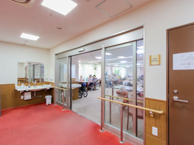 共有スペースで過ごす人々 廊下 広々とした食堂で、笑顔で過ごす利用者様の姿が見られます。明るく開放感のある設計は、ご利用者のコミュニケーションの場を提供しています。