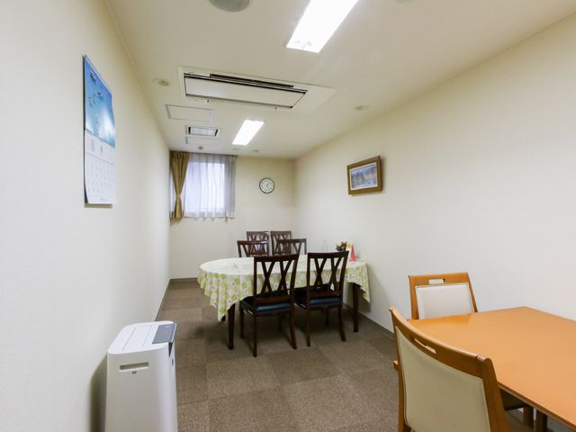 居室の食卓と椅子 共有スペース 清潔感あふれる居室で、ゆったりとした食事の時間を支えます。天井の照明が空間を明るく照らし出し、落ち着いた雰囲気です。