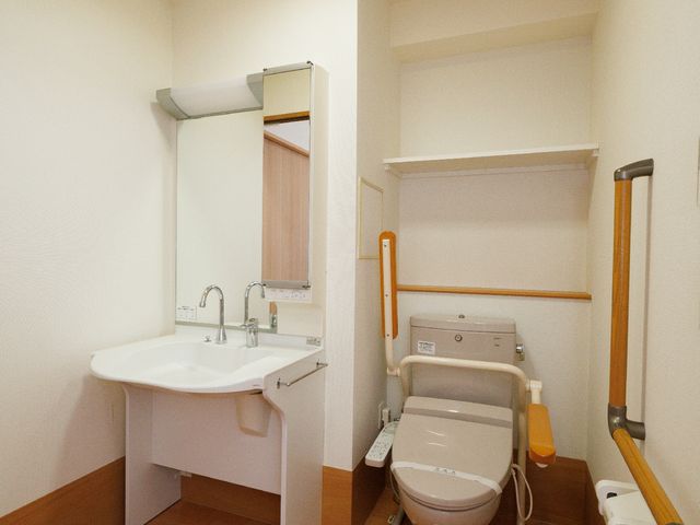 清潔感のある洗面トイレ空間 居室 手すり付きの洗面台とトイレが整った明るいスペースです。安全かつ快適な日々を過ごすための配慮が感じられる設備です。