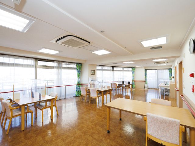 共用の明るい食堂 共有スペース 天井が高く、自然光が差し込む広い食堂です。丸い時計を中心としたシンプルな壁装飾が印象的で、ゆったりとした時間が過ごせそうです。