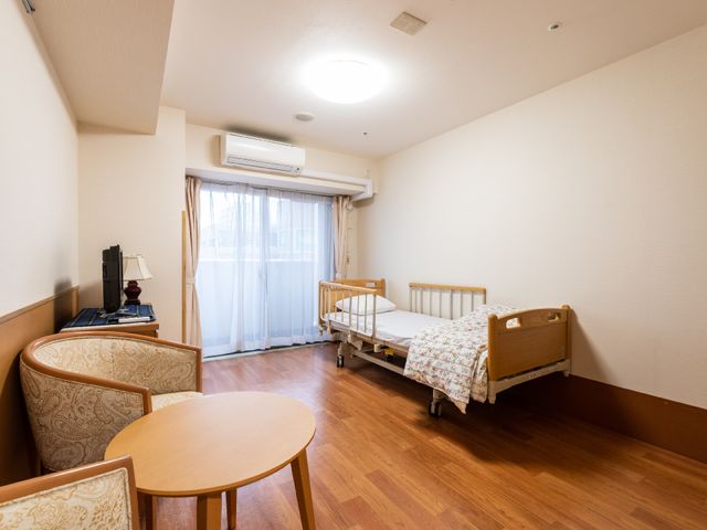 居室のベッドとテーブル 居室 広々とした居心地の良い個室です。窓からの自然光が心地よく、快適な日々を過ごせそうです。