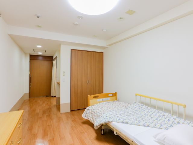 居室のベッドと入口 居室 広々とした居室にはシンプルなベッドが置かれ、すっきりとした雰囲気です。日々の暮らしを大切にした快適な空間です。