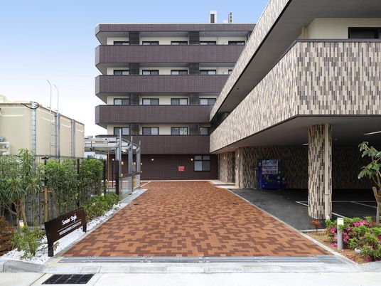 チェックのパジャマ姿でベッドに横になる高齢の女性の介護に当たる女性スタッフ。