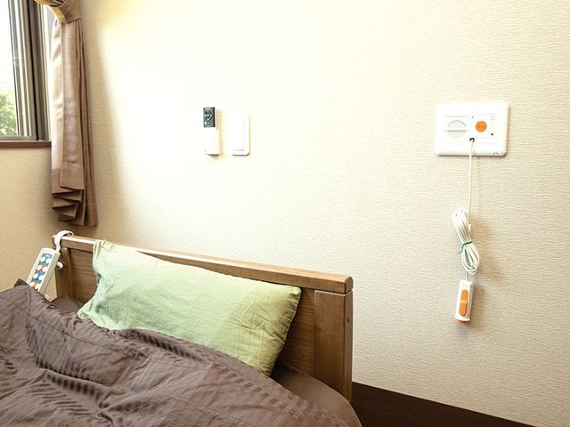 明るい居室のベッド周辺 居室   窓から自然光が入る、落ち着いた雰囲気の居室です。ベッド周りに呼び出し機器があり、安心して過ごしやすそうです。