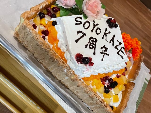 記念ケーキのテーブル 食堂   7周年を祝う大きなケーキが並び、果物や花で華やかに飾られています。行事やお祝いの雰囲気が伝わり、働く場のあたたかさを感じられます。