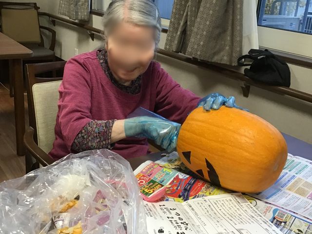 かぼちゃ作業の場面 リビング   窓から光が入る明るいリビングで、利用者の方がかぼちゃの作業をしています。食卓を使った活動の様子が伝わり、交流の場としても使いやすそうです。