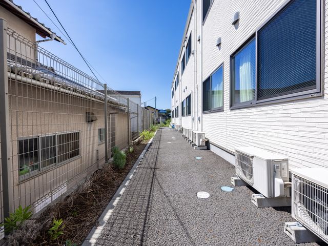 白い壁の建物と散歩道 外観 清潔感溢れる白い壁の建物の横には、散歩やリフレッシュに最適な遊歩道が整備されています。