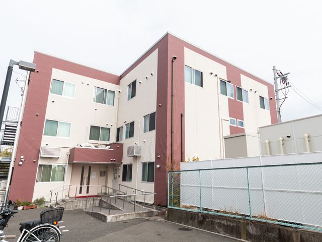 赤と白の外壁の建物 外観 モダンなデザインの建物前にはバリアフリーのアプローチがあり、どなたも安心してお過ごしになれる環境が整っています。