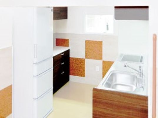 リビングの近くにキッチンが設置されている。キッチンには白い冷蔵庫が置かれている。壁は茶色と白色のツートンカラーとなっている。