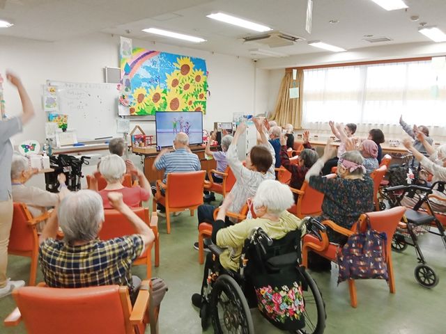 元気な活動中の居室 居室 たくさんの方々が集まり、明るい雰囲気の中で体操を楽しんでいます。自然光が差し込む快適な空間です。