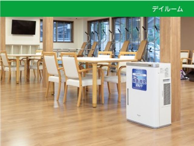 明るいデイルーム ダイニングルーム   窓から光が入る明るい空間で、木目調の床とテーブル席がゆったり配置されています。くつろぎながら食事や会話をしやすい雰囲気です。