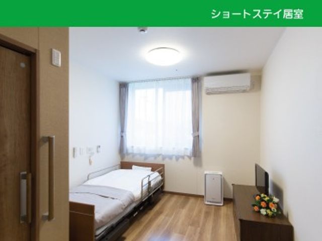 明るい居室のベッド横 居室   窓から自然光が入る、明るくすっきりした居室です。ベッドやテレビが配置され、落ち着いて過ごしやすい印象です。