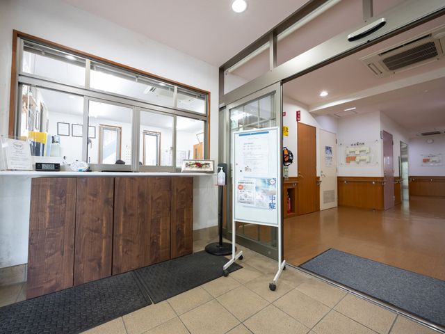受付カウンターのある出入口 エントランス   明るい出入口に受付カウンターがあり、案内掲示も見やすいです。段差の少ない導線で、来訪者が通りやすそうです。