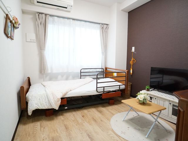 居室の一角 居室 整えられた居室で、シックな壁紙と木の家具が落ち着いた雰囲気を醸し出しています。窓から自然光が差し込む暖かい空間です。
