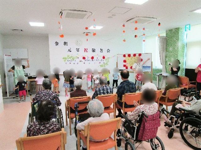 イベントを楽しむ多目的室 通所 広々とした室内で椅子に座る方々がイベントを楽しまれています。壁には季節の装飾が施され、にぎやかな雰囲気が感じられます。